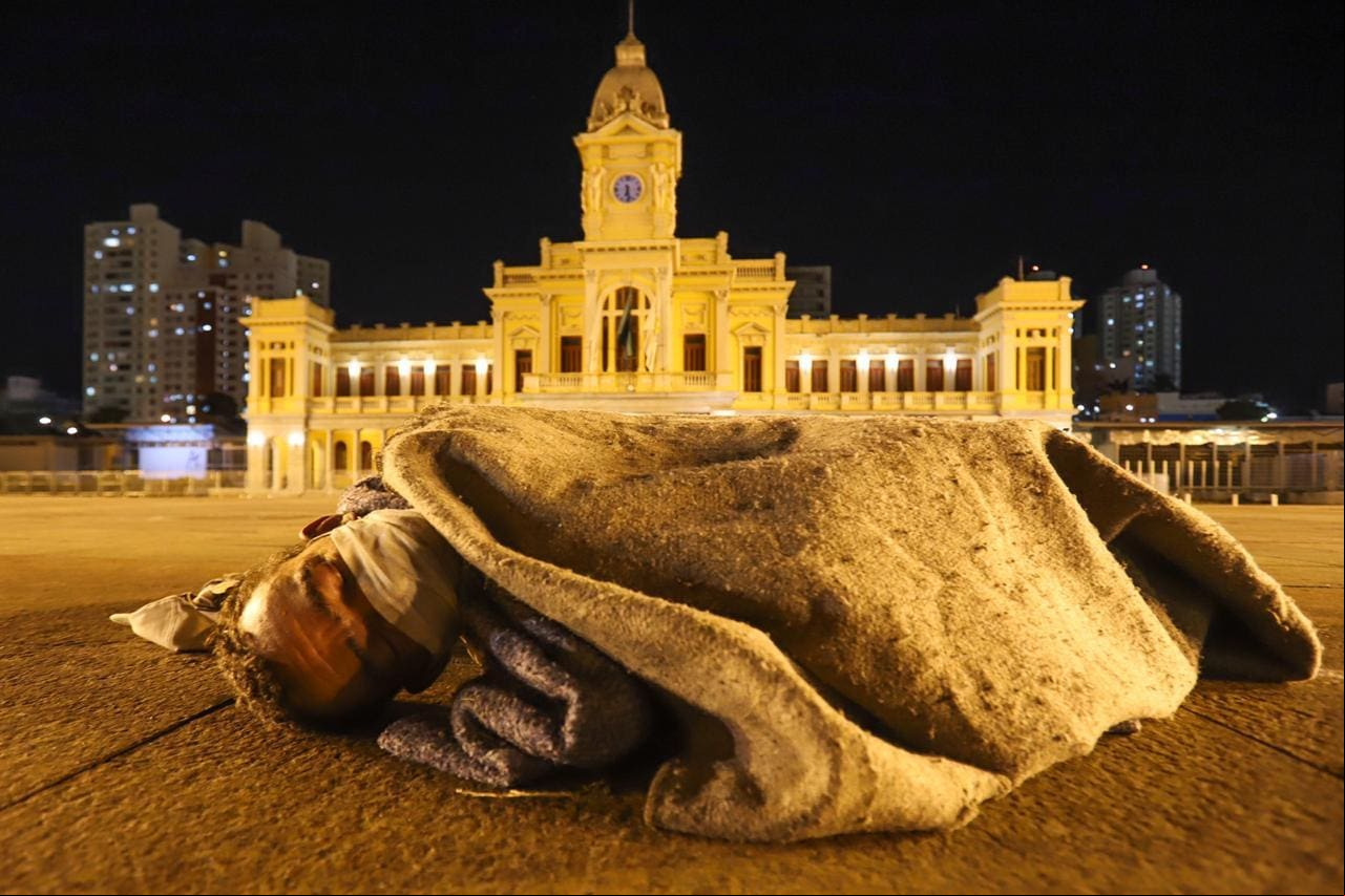 Morador de rua com máscara contra o COVID-19 se protege do frio na Praça da Estação